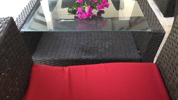 A wicker chair with a red cushion and a glass-top table with a bouquet of pink flowers.
