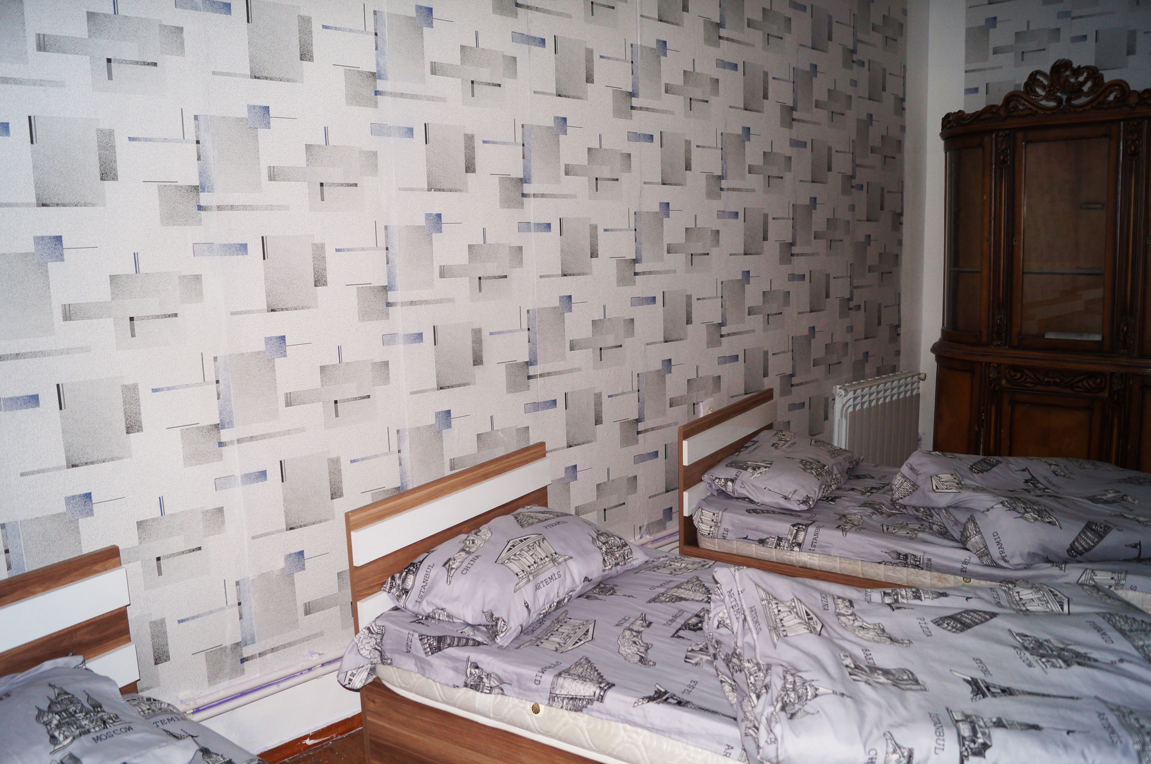A room with two beds, a wooden headboard, a patterned wall, and a wooden cabinet.