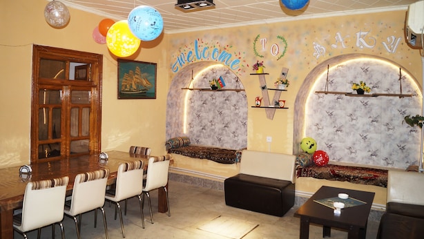 A room with a wooden dining table, white chairs, a sofa, and a small table with a decorative item. - Pegasus Hostel (Baku)