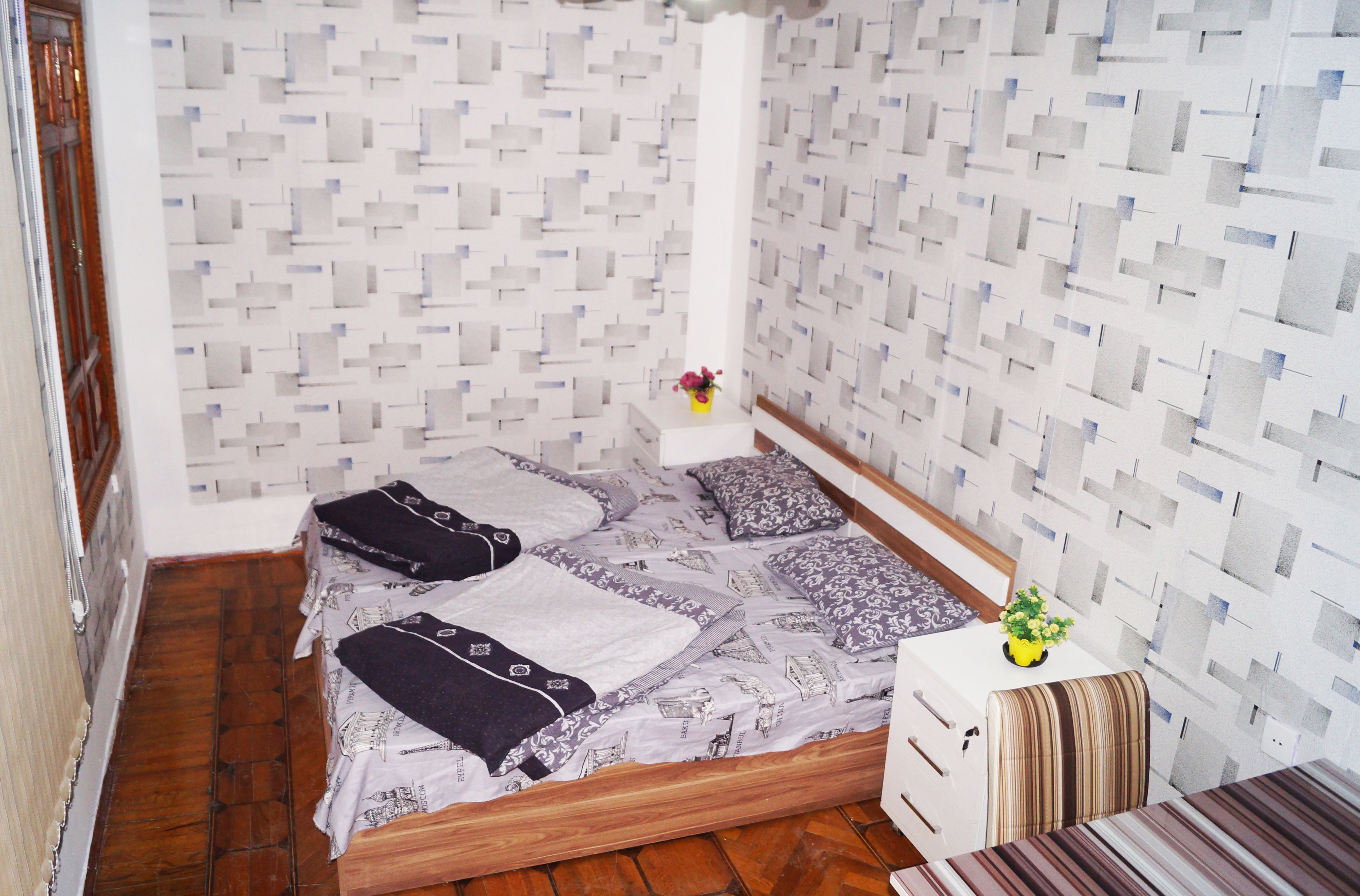A small bedroom with a bed, a nightstand, a chair, and a wall with a geometric pattern.