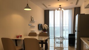 A modern dining area with a glass table, six chairs, a chandelier, and a refrigerator. - Mins Apartment - Vinhome Golden River (Ho Chi Minh City)