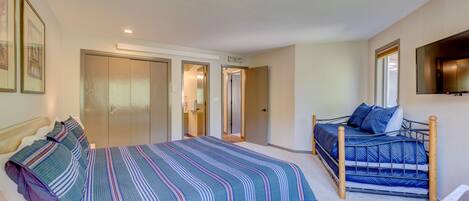 Un dormitorio con una cama grande, una cama más pequeña y un armario. Hay un televisor en la pared y una puerta que da a otra habitación.