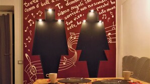 A dining area with a table set for two, a chair, and a wall with a musical note design and text. - B&B Villa Cinque Pini (Casamicciola Terme)