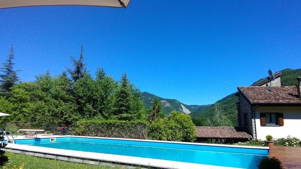 Una piscina con vista su una montagna, circondata da alberi e una casa con tetto in tegole.