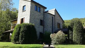 Un edificio in pietra con tetto spiovente, circondato da siepi curate e un cielo sereno.