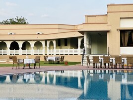 Zona de piscina con mesas y sillas, una piscina e edificio con arcos y balcón.