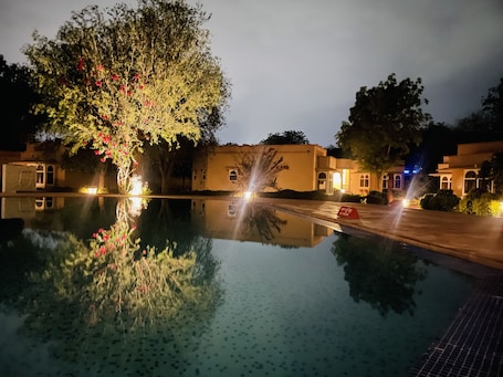 A nighttime view of a hotel with a swimming pool reflecting the surrounding trees and buildings.