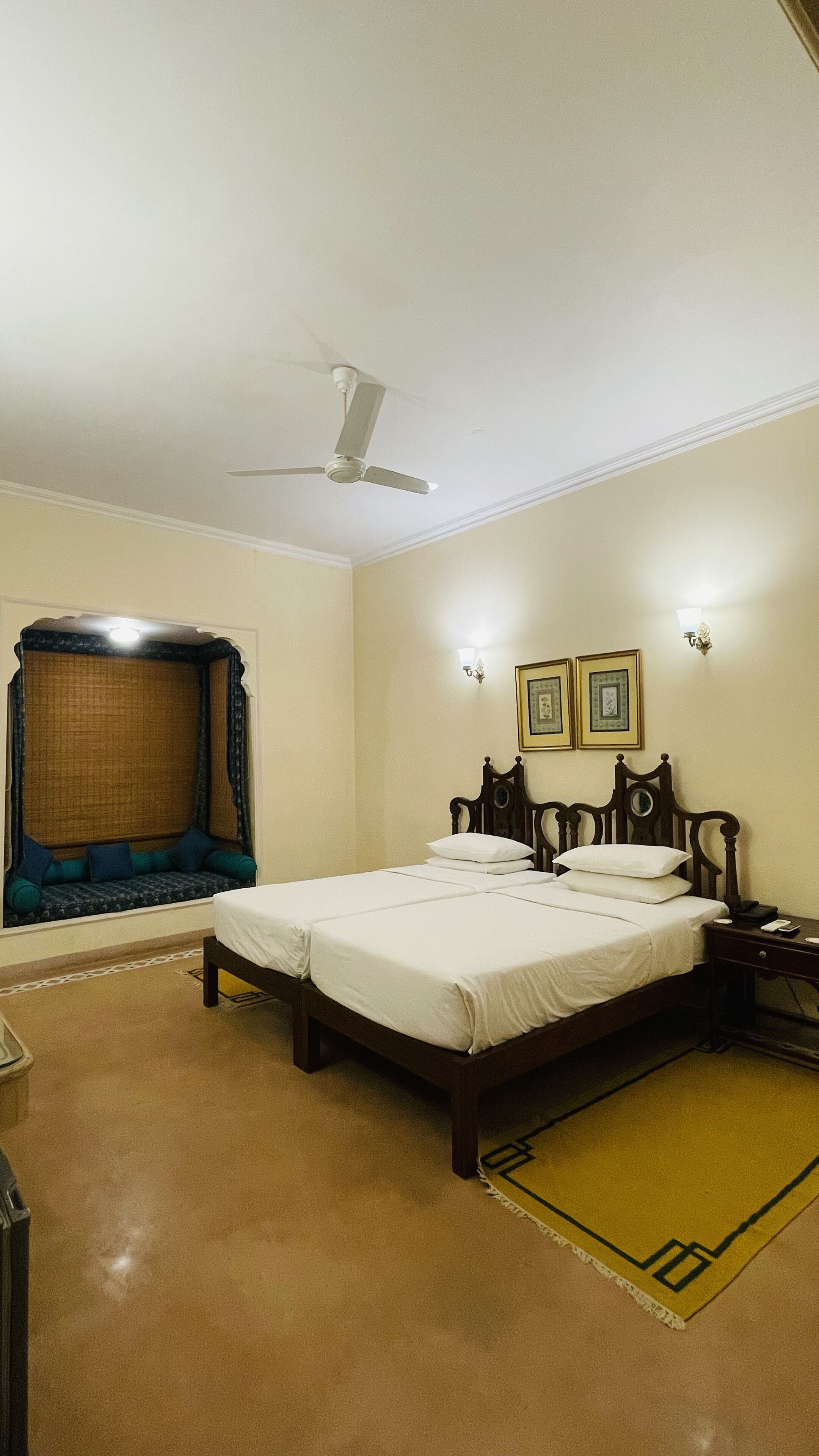Un dormitorio con una cama doble, ventilador de techo, mesita de noche con teléfono y lámpara de pared.