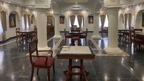 Un vaste espace dédié à la salle à manger, doté d’un sol en marbre, de tables et de chaises en bois, ainsi que de colonnes décoratives.