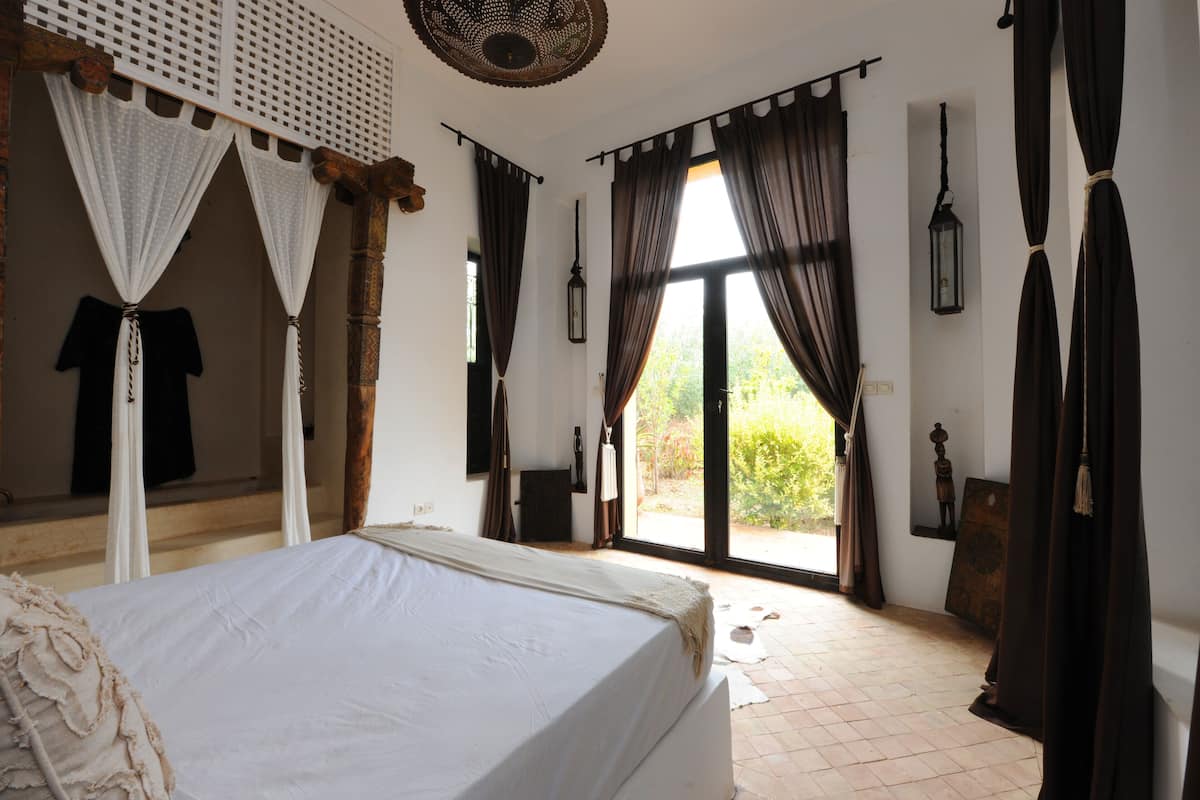 Quarto com cama, cortinas, janela e porta.