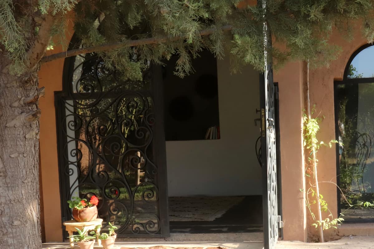 Entrada de um edifício com portão de ferro forjado, plantas em vasos e tapete de azulejos.