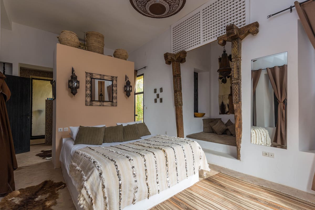 Quarto com uma cama grande, um sofá, um espelho e um pilar de madeira decorativo.