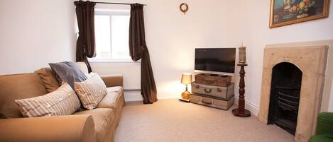 A living room with a beige sofa, a television, a fireplace, and a painting on the wall.