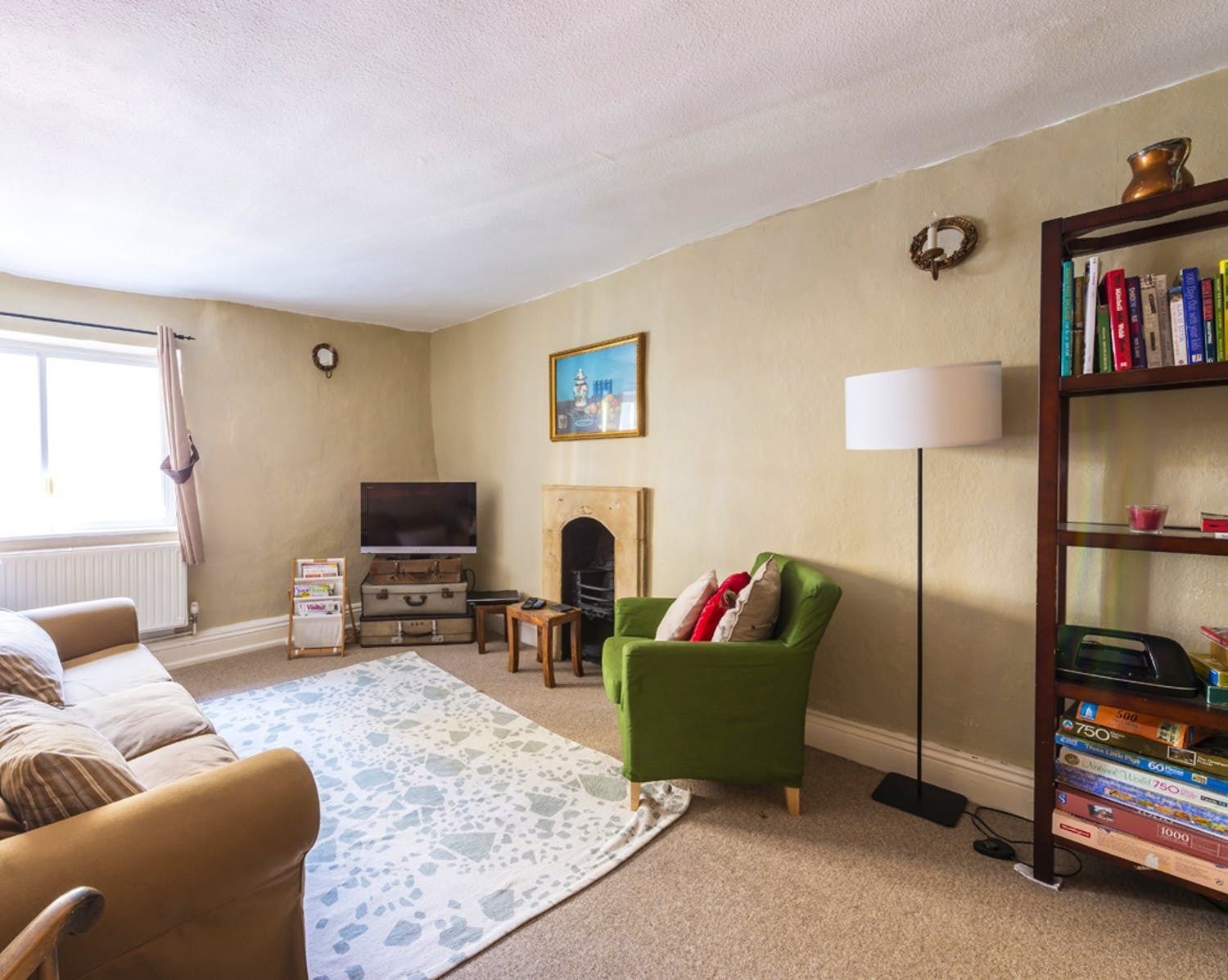A living room with a sofa, a green armchair, a fireplace, a bookshelf, and a television.