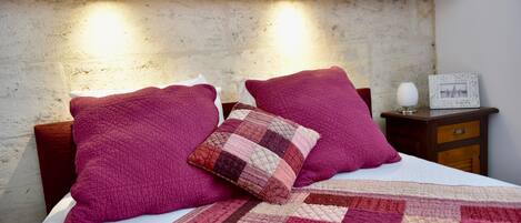 A bed with a quilt and two pillows, a bedside table with a lamp, and a framed picture on the wall.