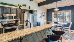 Une cuisine moderne dotée de plans de travail en granit, d’appareils électroménagers en acier inoxydable et d’un coin repas avec une table et des chaises en bois.