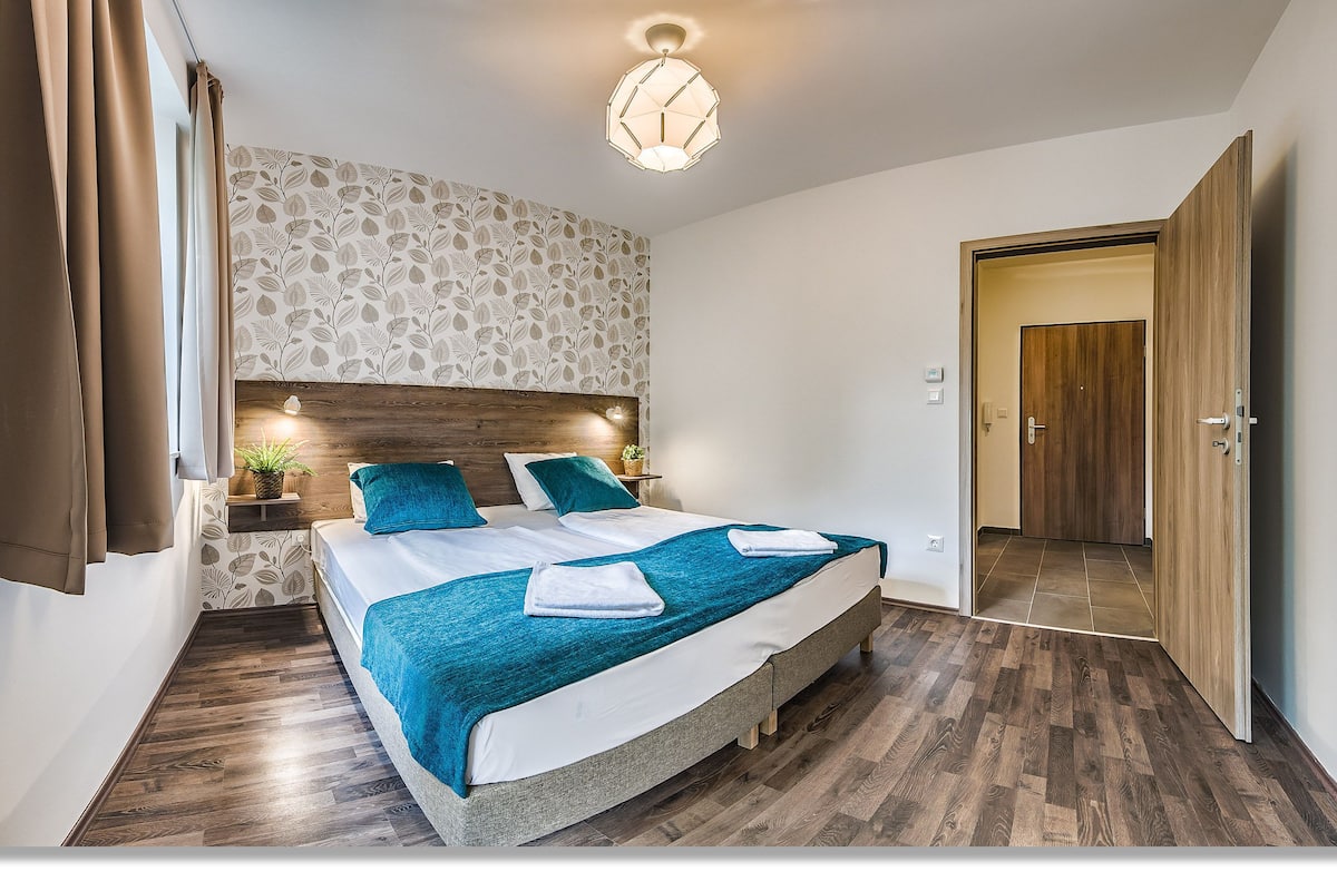 Une chambre à coucher comprenant un lit, une table de chevet, une lampe fixée au mur et une porte donnant sur une autre pièce.