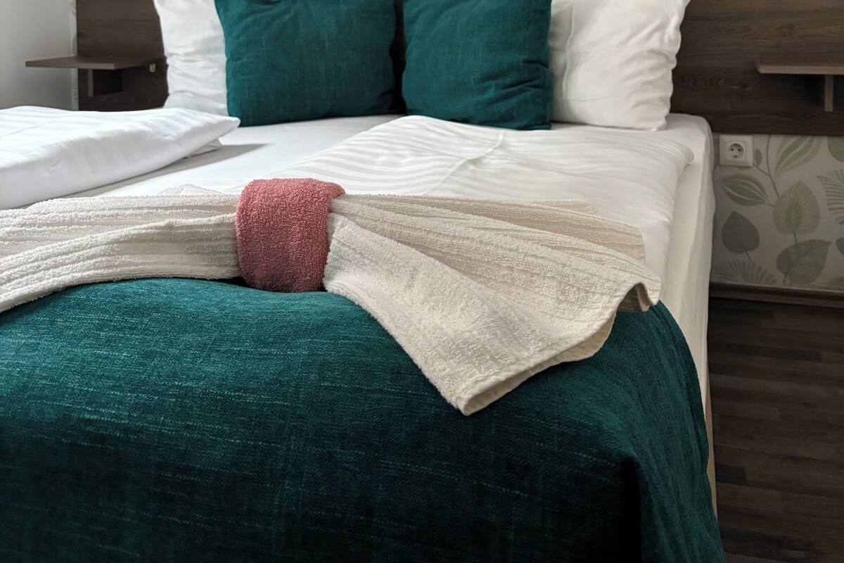 Un lit bien fait, avec une tête de lit en bois, des oreillers blancs et turquoise, et une couverture turquoise et blanche.