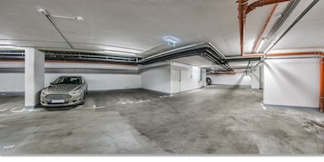 Uma garagem de estacionamento com vários níveis, pisos e paredes de concreto, tubulações e dutos visíveis, e um carro estacionado em uma das vagas.