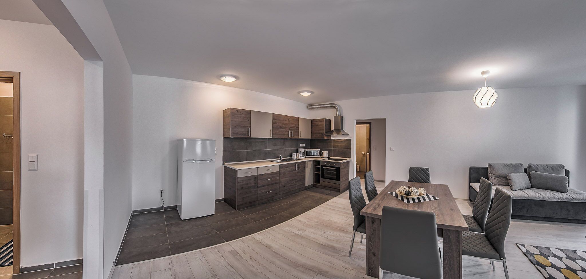 Una cocina moderna con armarios de madera oscura, un refrigerador blanco y una zona de comedor con mesa y sillas de madera.