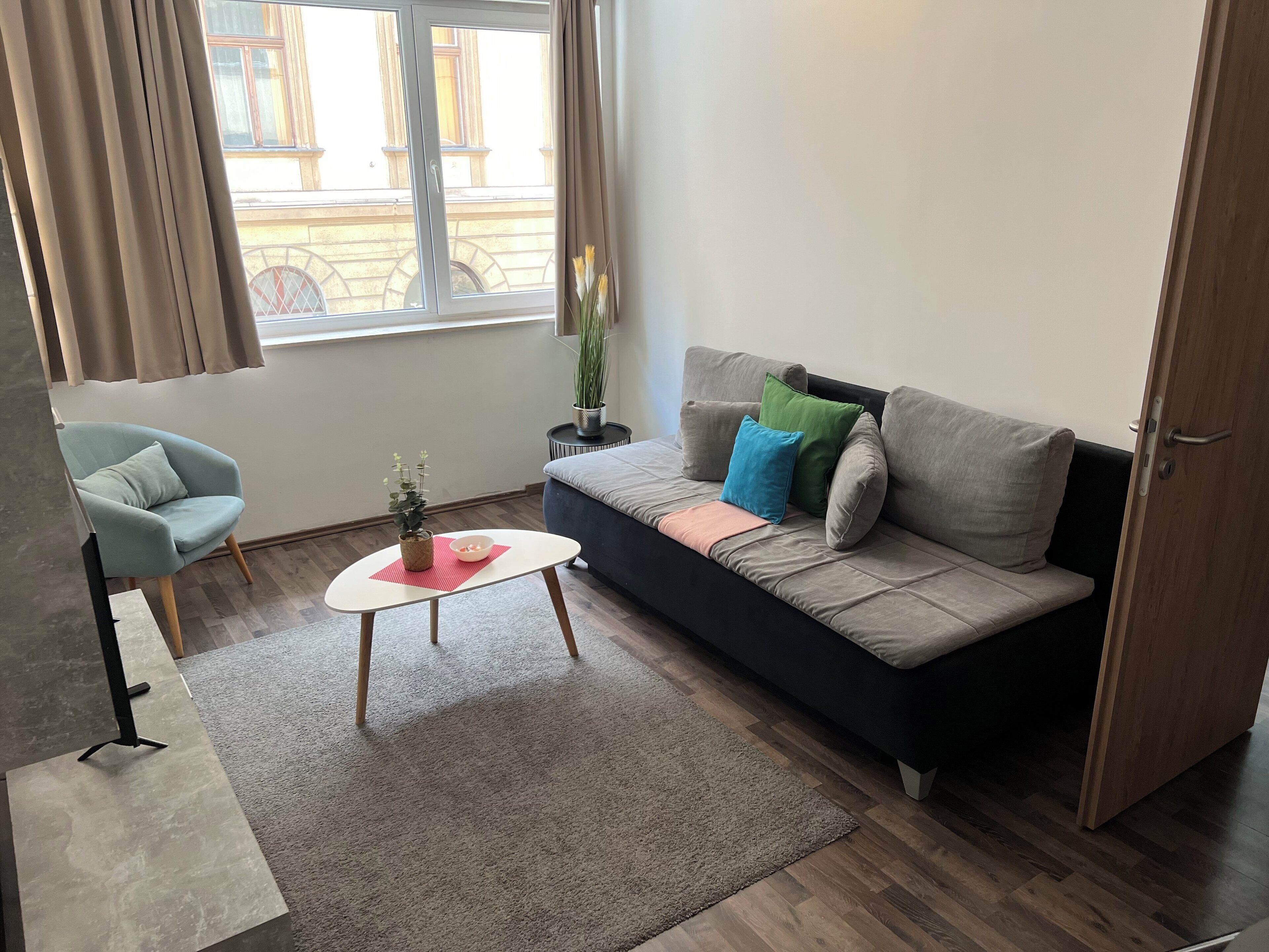Un salon avec un canapé, un fauteuil, une table basse et une fenêtre avec des rideaux.
