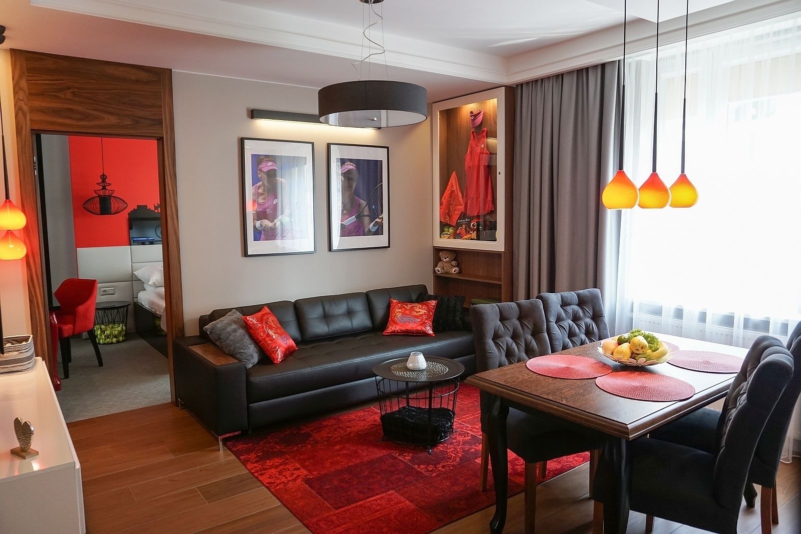 Ein modernes Wohnzimmer mit einer schwarzen Couch, roten Kissen, einem Esstisch mit Stühlen und einem roten Teppich.