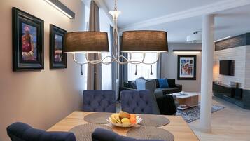 Un comedor moderno con una mesa de madera, sillas tapizadas en azul y un frutero. Hay cuadros en la pared y una lámpara de araña encima.