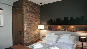 A hotel room with a brick accent wall, a city skyline mural, a neatly made bed with white linens, a bedside table with a lamp, and a small shelf with decorative items. - AGA Tenis Apartments by Radwanska (Kraków)