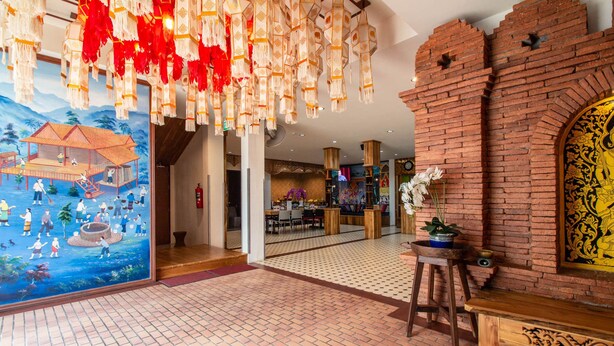 A spacious lobby with a traditional mural, a brick wall with intricate carvings, and hanging decorations. - Anumat Premium Budget Hotel (Chiang Mai)