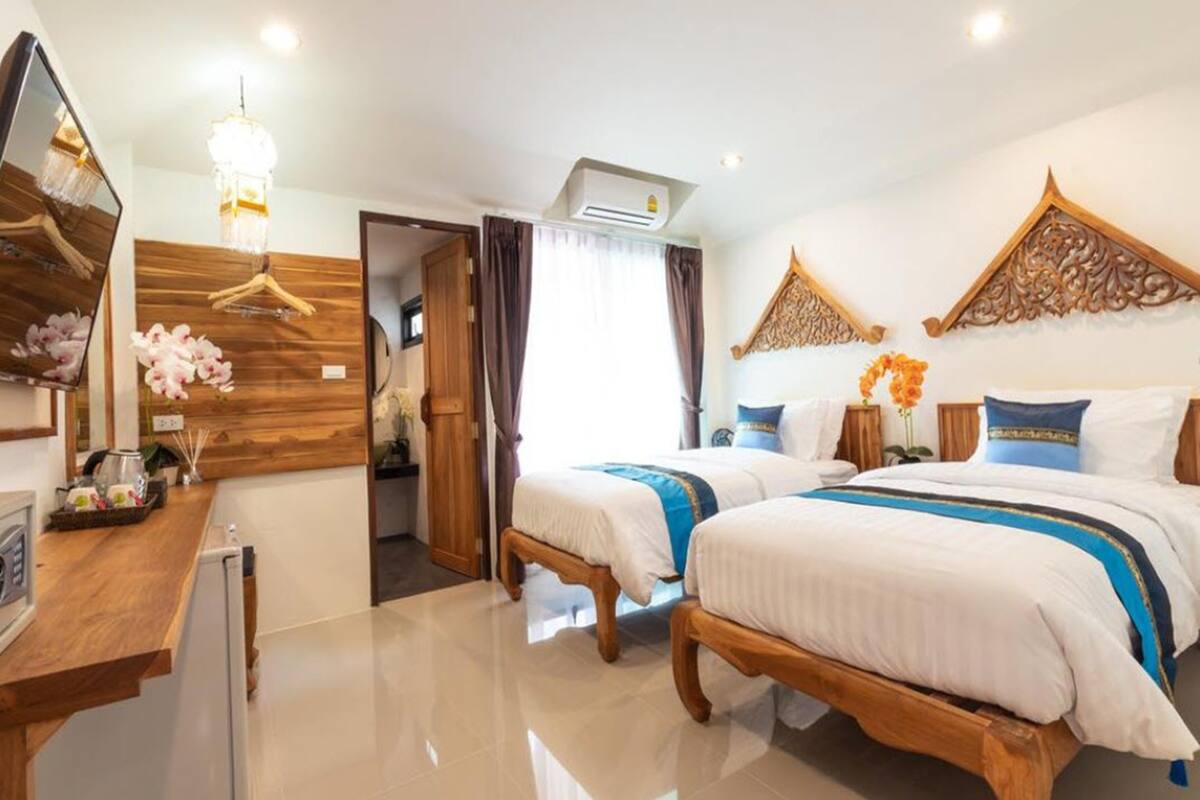 A hotel room with two beds, a wooden desk, a mirror, and a chandelier.