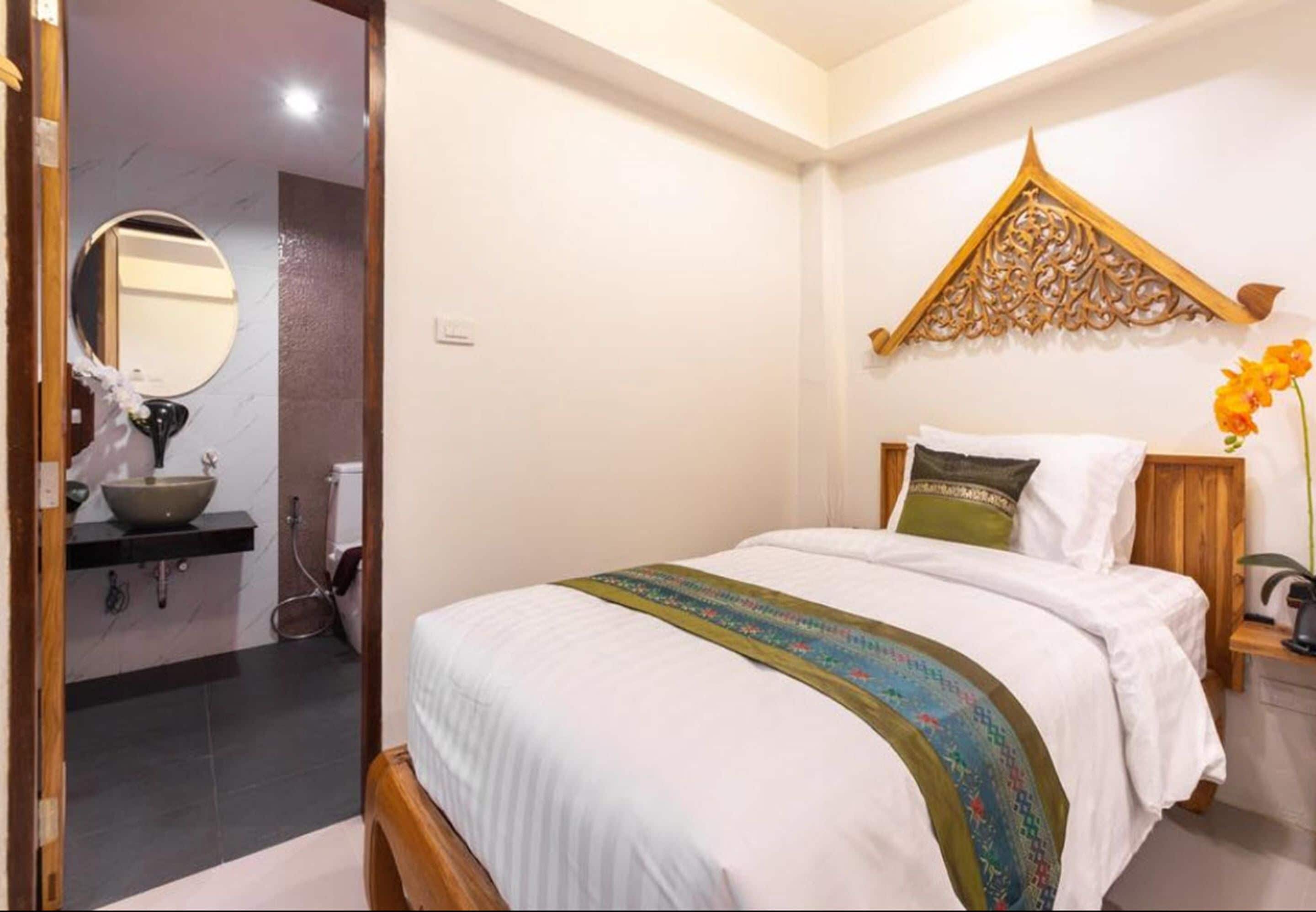 Quarto com cama, cabeceira de madeira, um ornamento na parede e mesa de cabeceira com abajur.