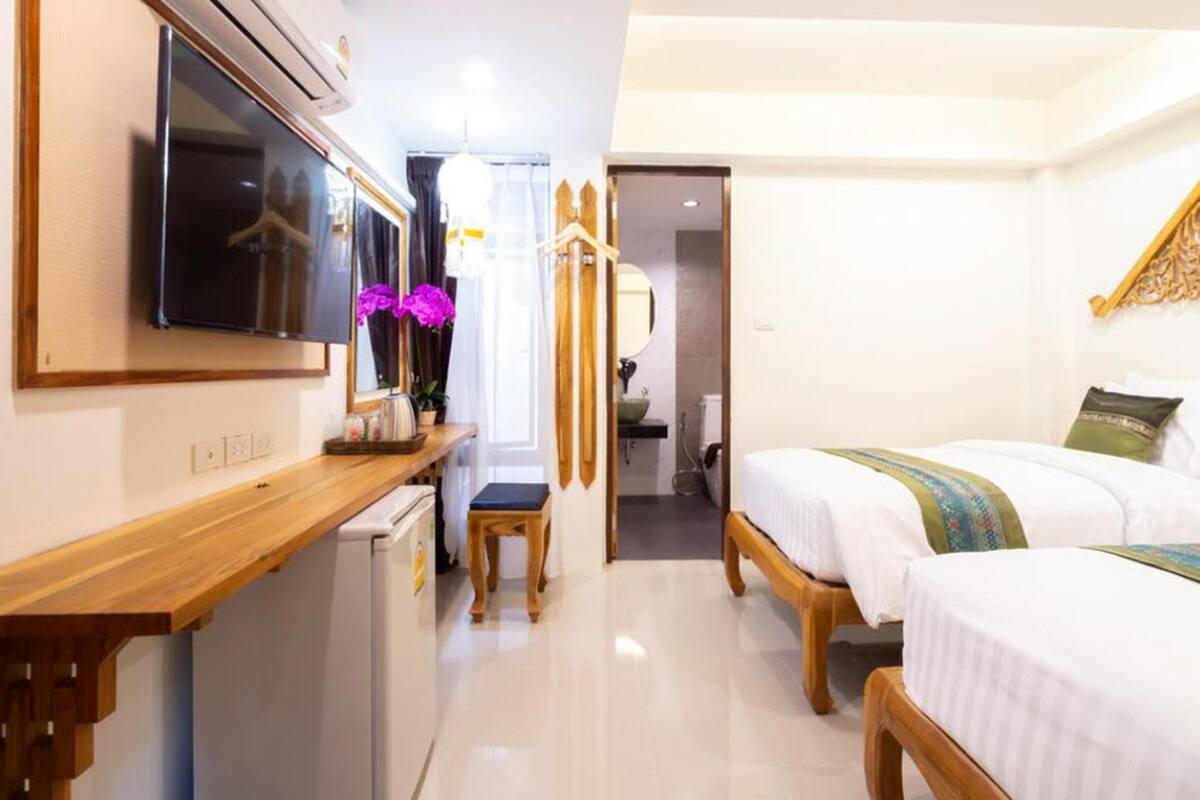 A hotel room with a wooden desk, a television, a bed with a green and blue bedspread, and a small bathroom visible through an open door.