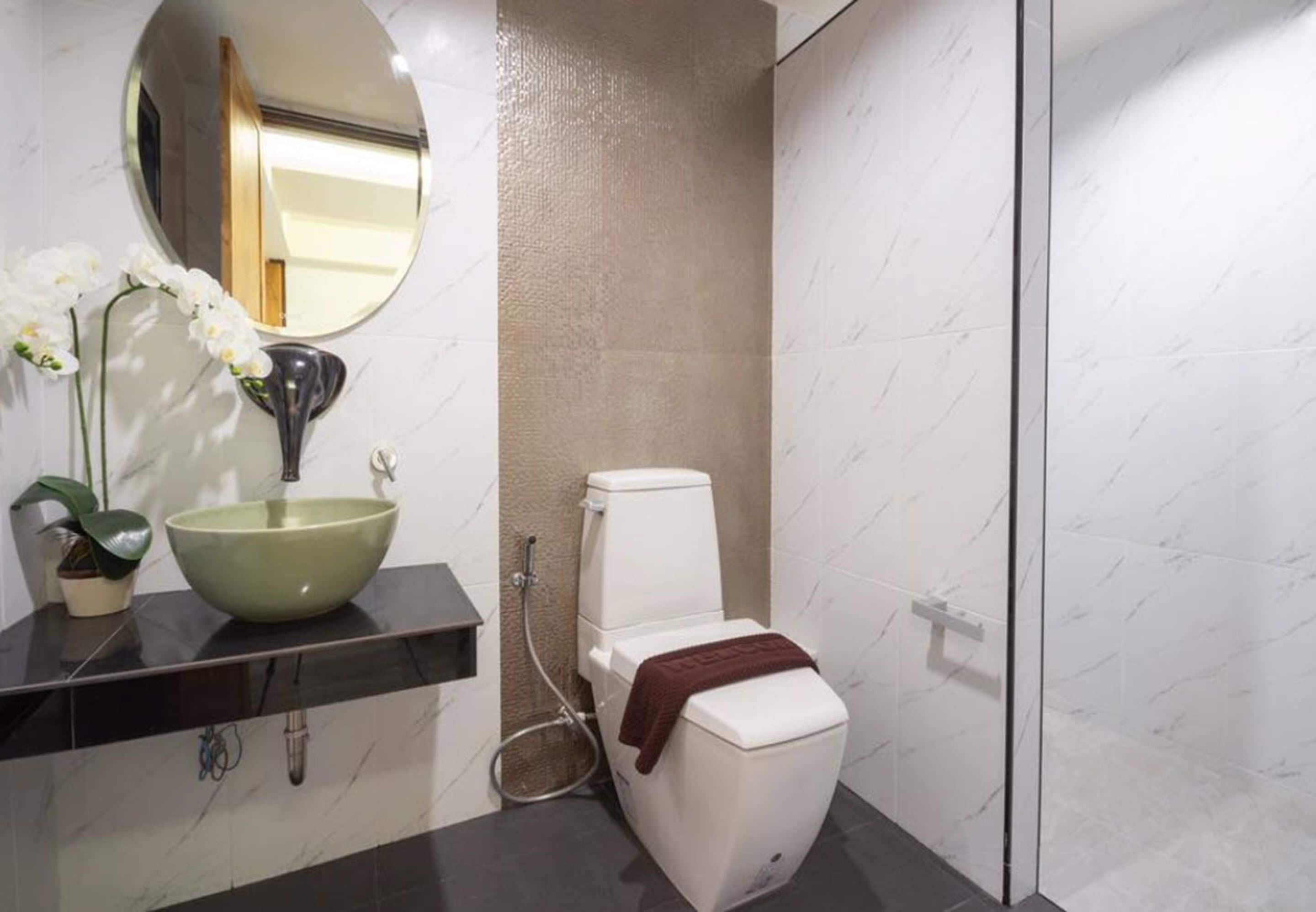 Et badeværelse med et rundt spejl, en grøn vask, toilet og bruseområde.