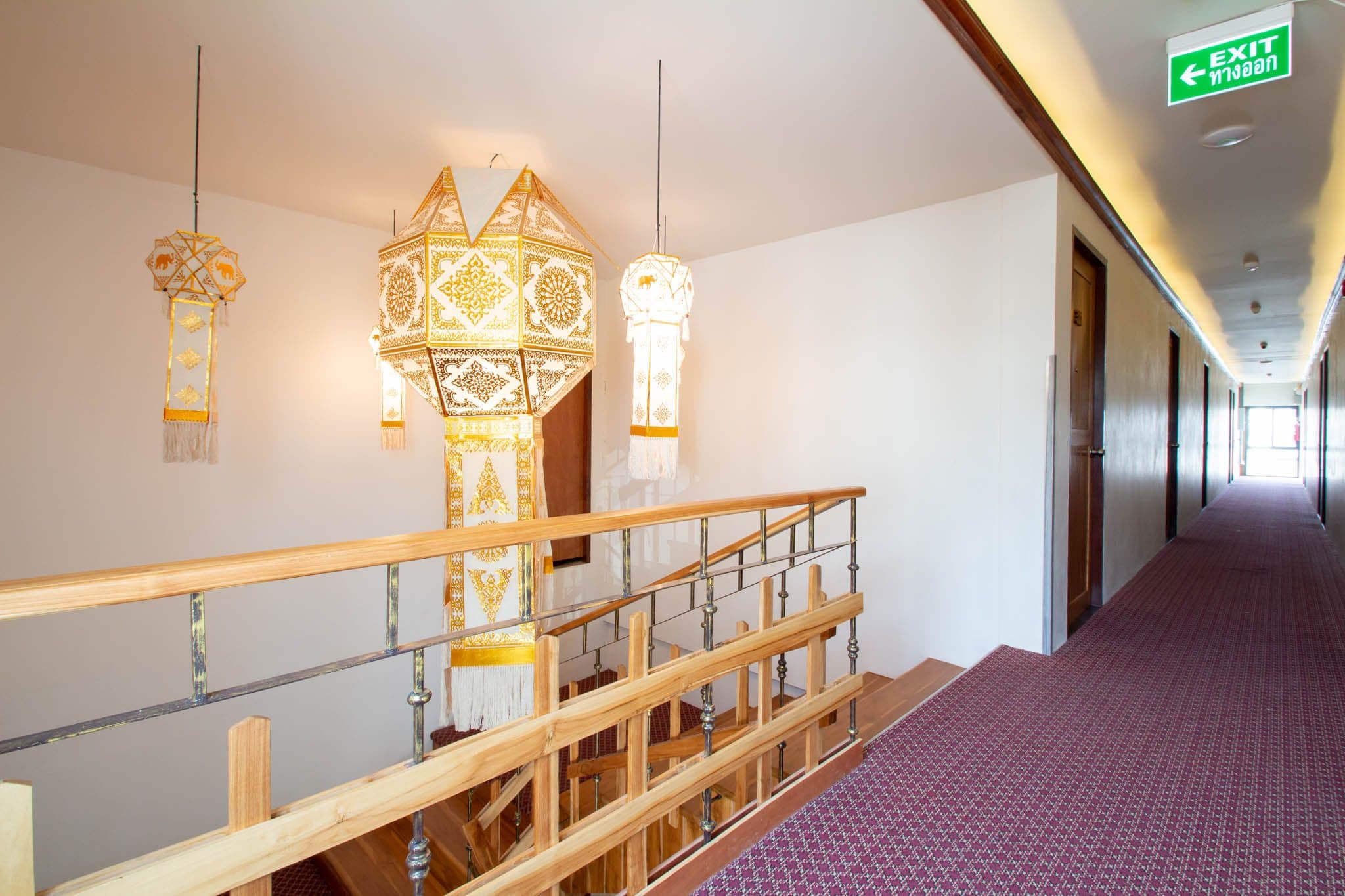 A hallway with patterned wall hangings, a wooden railing, and a carpeted floor.
