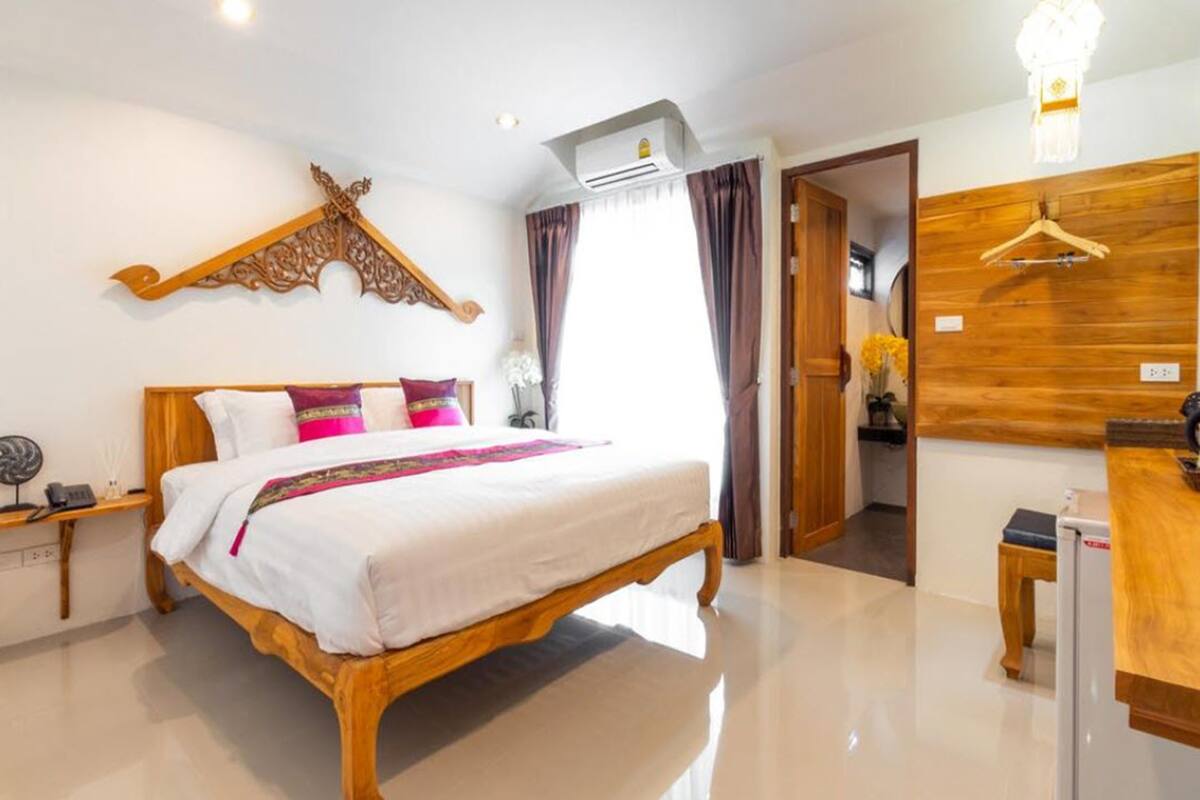 A well-lit hotel room with a large bed, wooden headboard, and a wooden wardrobe.