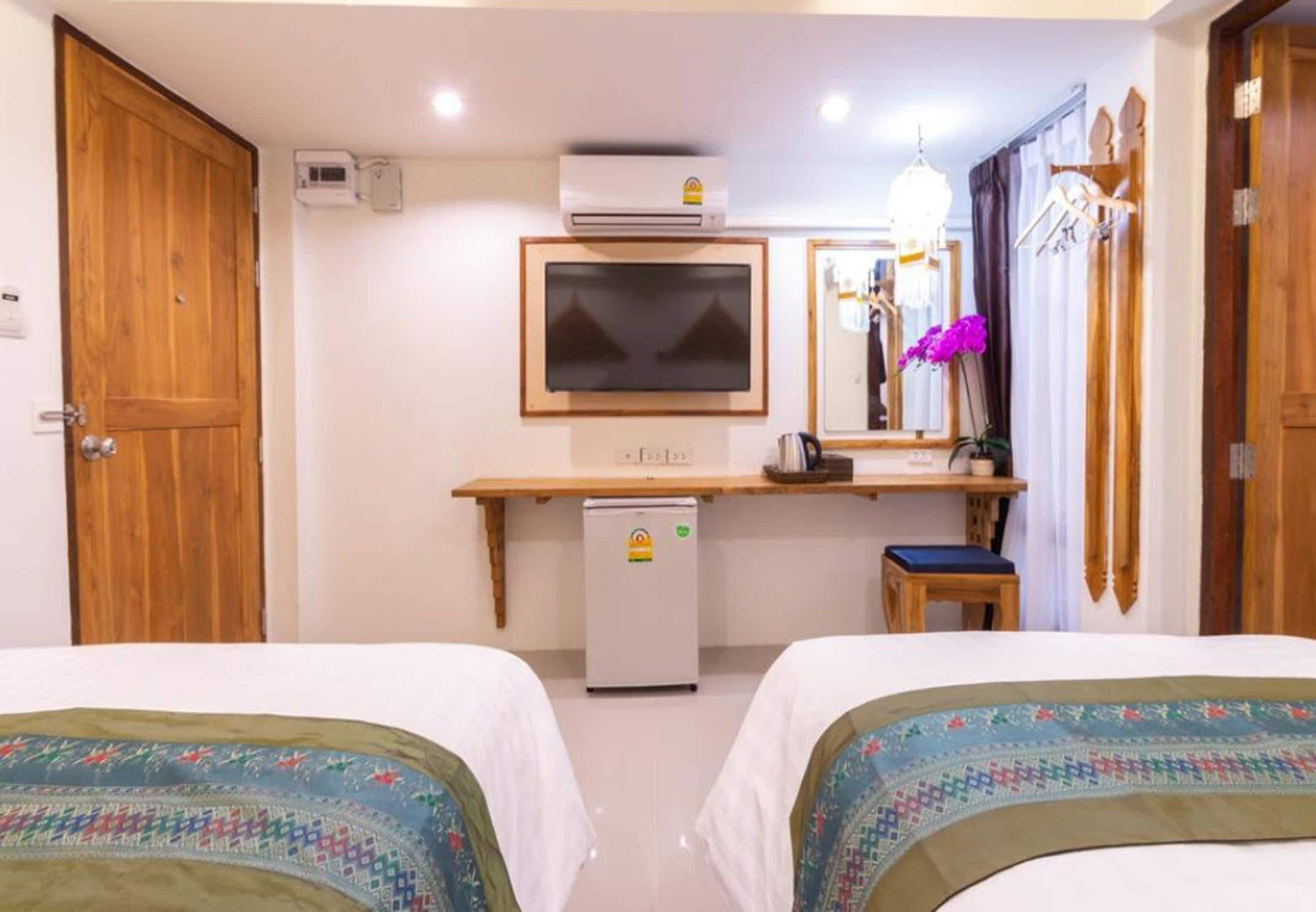 A hotel room with two beds, a small desk with a chair, a television, a mini-fridge, and a mirror.