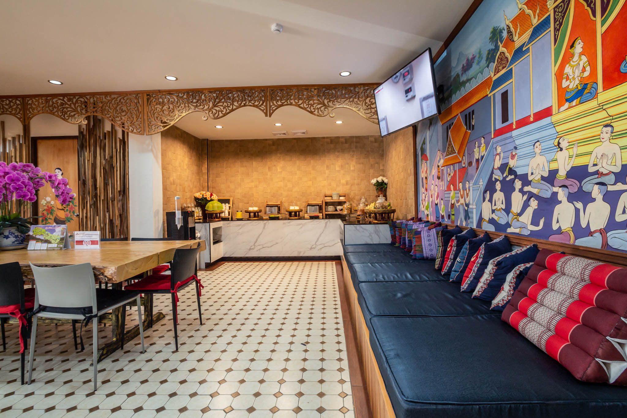 A hotel lobby with a reception desk, seating area, and a wall with traditional artwork.