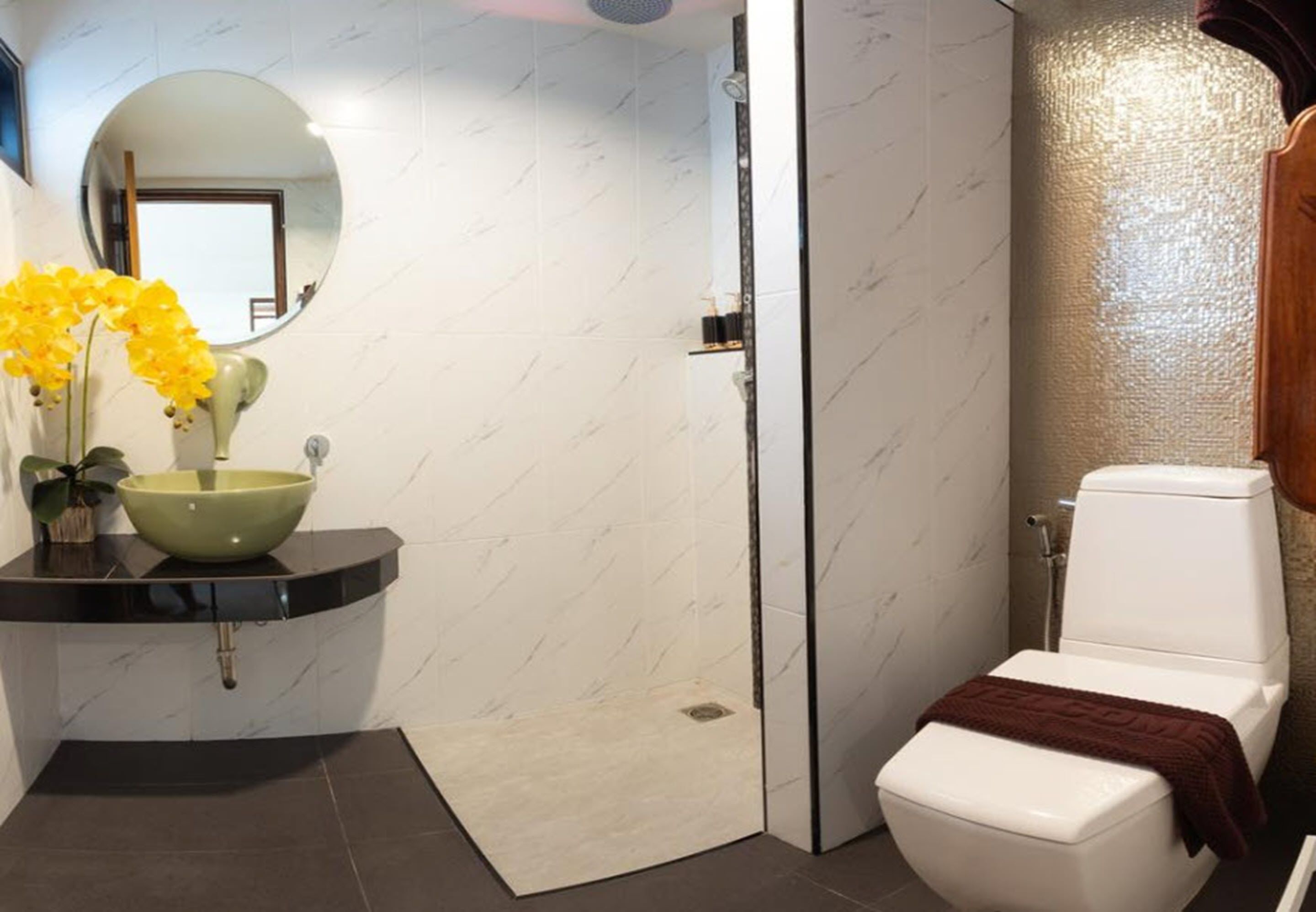 Een badkamer met een wastafel van wit marmer, een groene komgootsteen, een wit toilet en een douchegedeelte.
