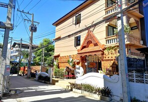 Una casa tradicional tailandesa con un porche decorativo, un pequeño santuario y un jardín con plantas y una estatua.