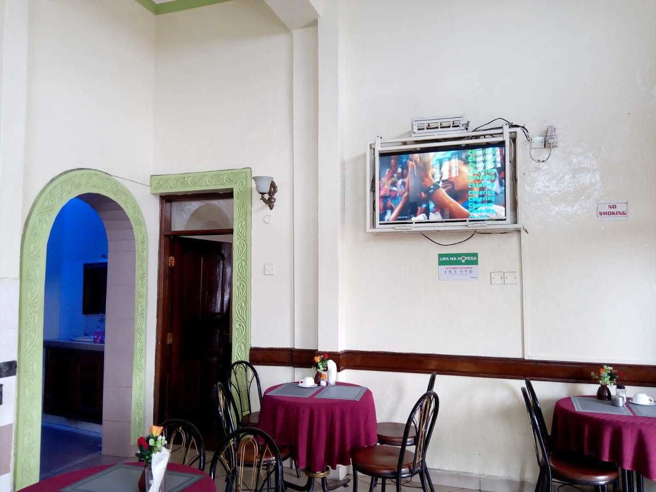 A restaurant with a TV mounted on the wall displaying a sports event, a sign prohibiting smoking, and a table with a red tablecloth.