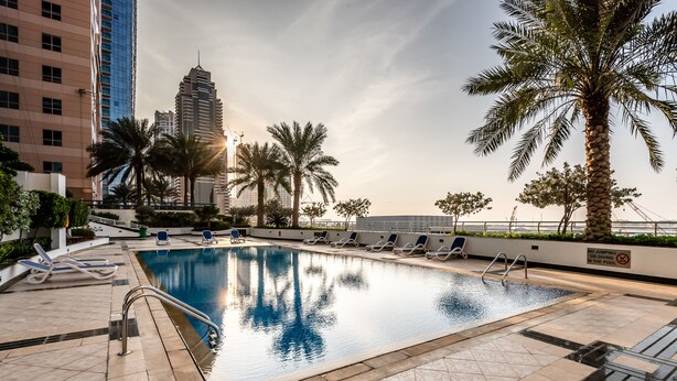 A rooftop swimming pool with lounge chairs, palm trees, and a cityscape in the background. - Peaks Apartments Dubai Marina (Dubai)