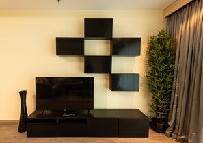 A modern living room with a flat-screen TV on a black entertainment unit, a decorative wall art piece, and a tall green plant.