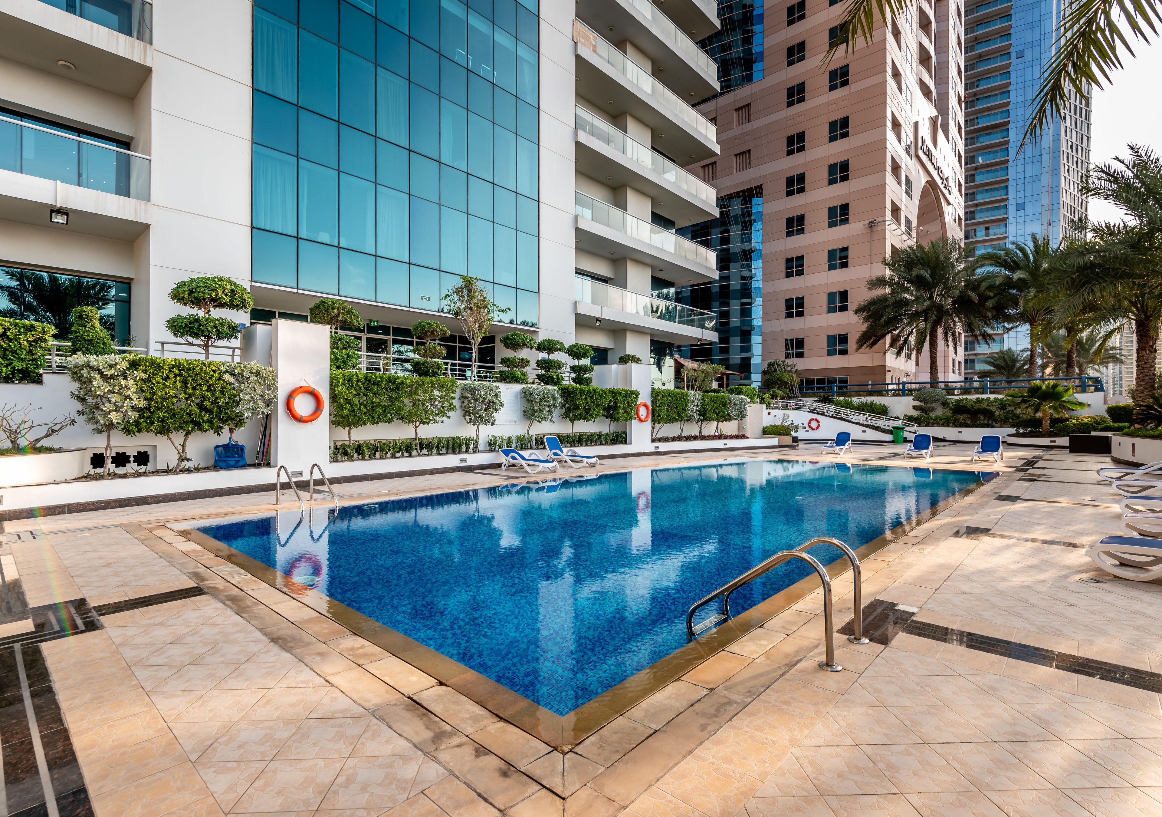Piscina rodeada por edifícios modernos, com céu claro e sem pessoas à vista.