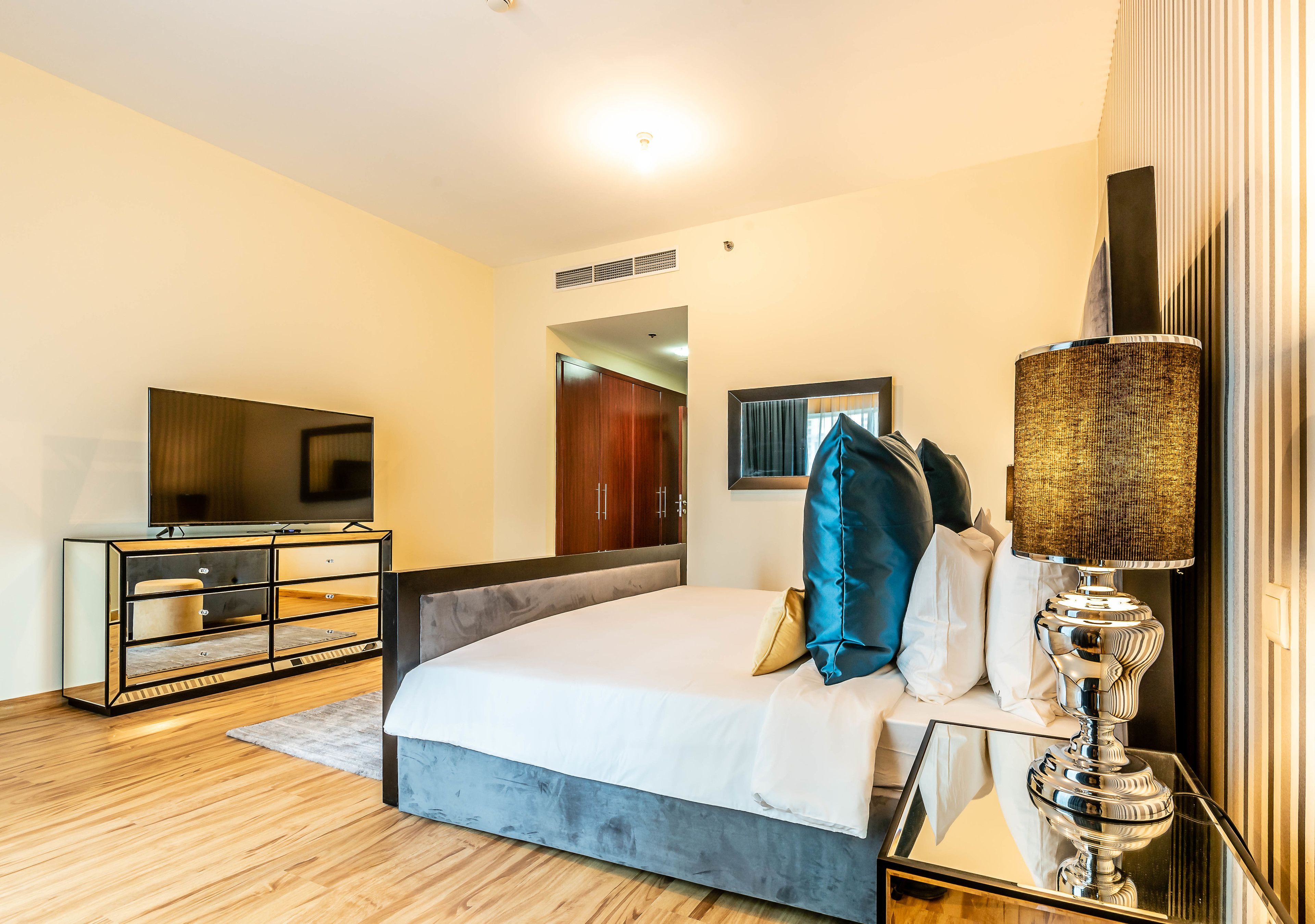A modern hotel room with a large bed, a TV, a dresser, and a lamp.