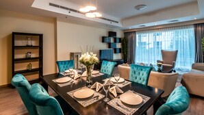 A dining area with a dark wooden table set for six, surrounded by teal upholstered chairs. - Peaks Apartments Dubai Marina (Dubai)
