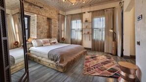 A bedroom with a large bed, a wooden floor, a stone wall, and a patterned rug. - Casa Sur Antalya (Antalya)