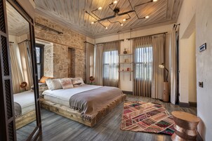 Ein Schlafzimmer mit einem großen Bett, Holzboden, Steinwand und einem gemusterten Teppich.