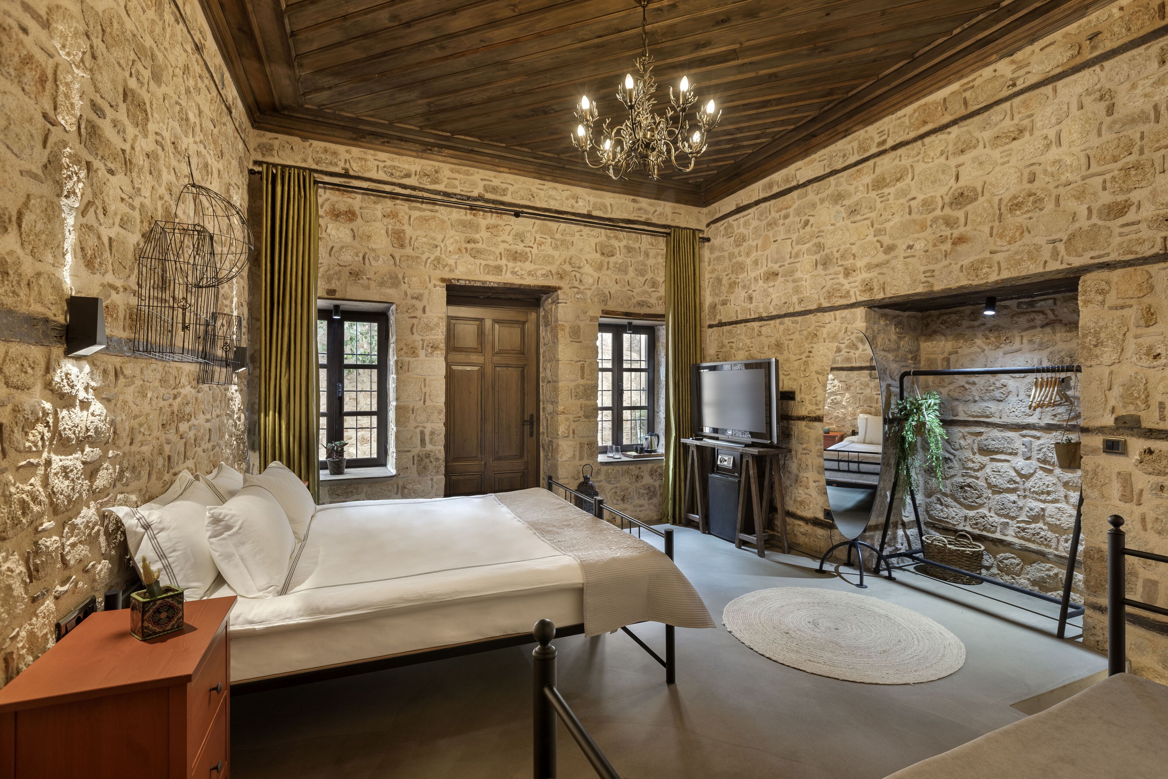 A rustic stone-walled room with a bed, a chandelier, a television, and a stone fireplace.