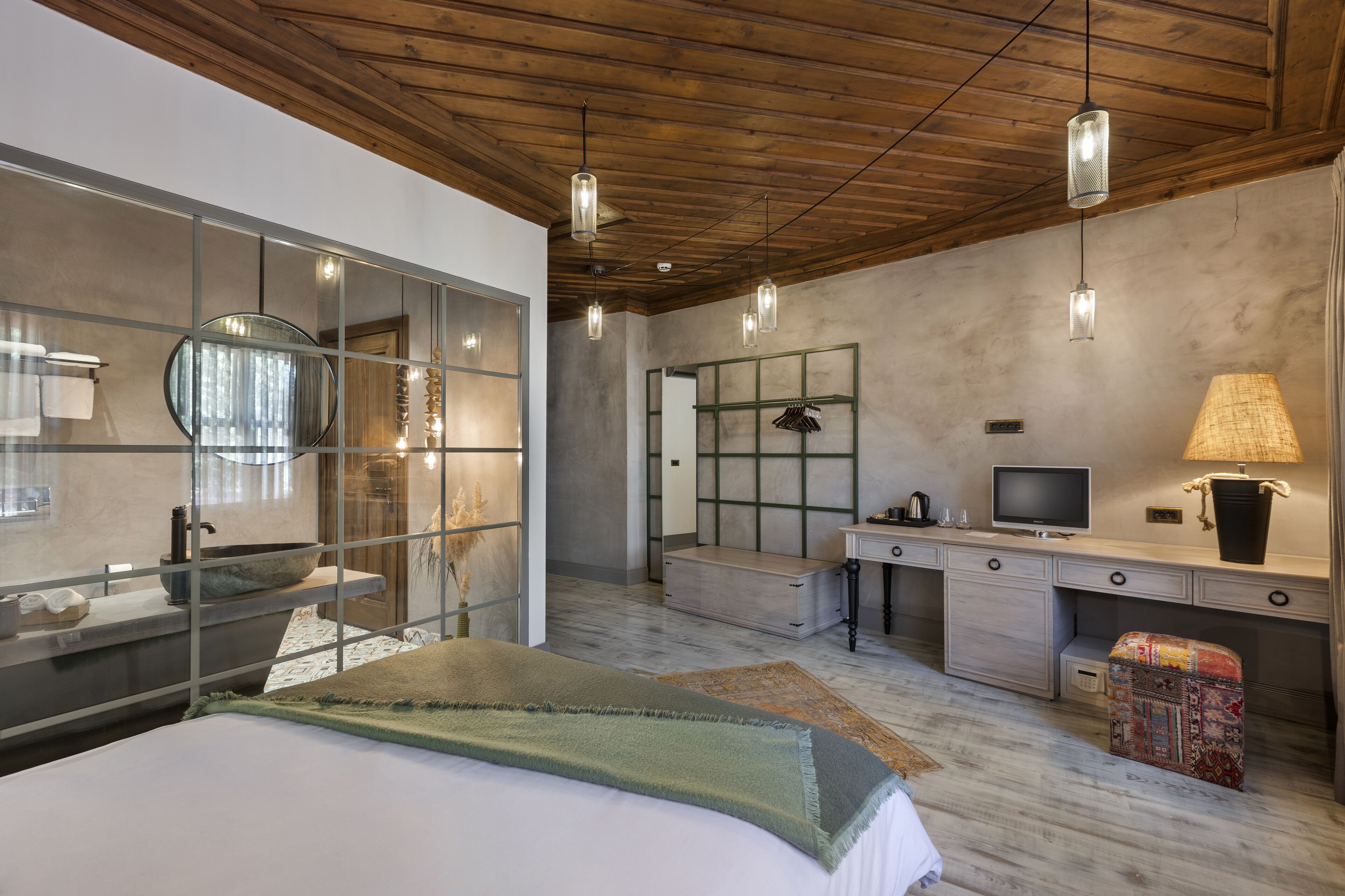 A modern bedroom with a large bed, a vanity with a mirror, a television, and a desk with a lamp.