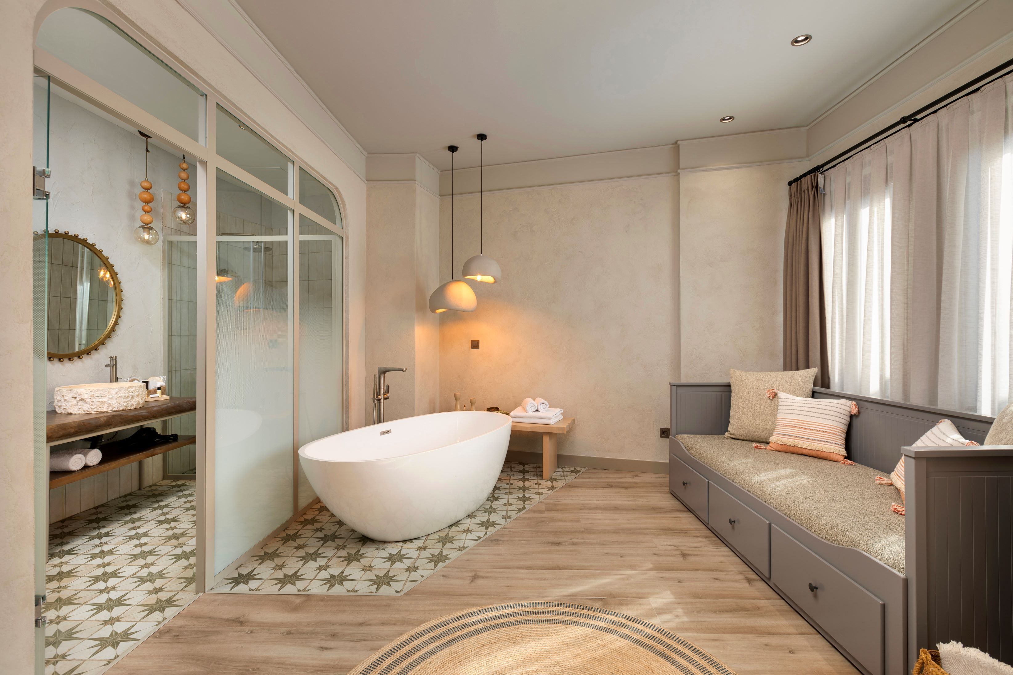A modern bathroom with a freestanding bathtub, a vanity with a mirror, and a seating area with cushions.